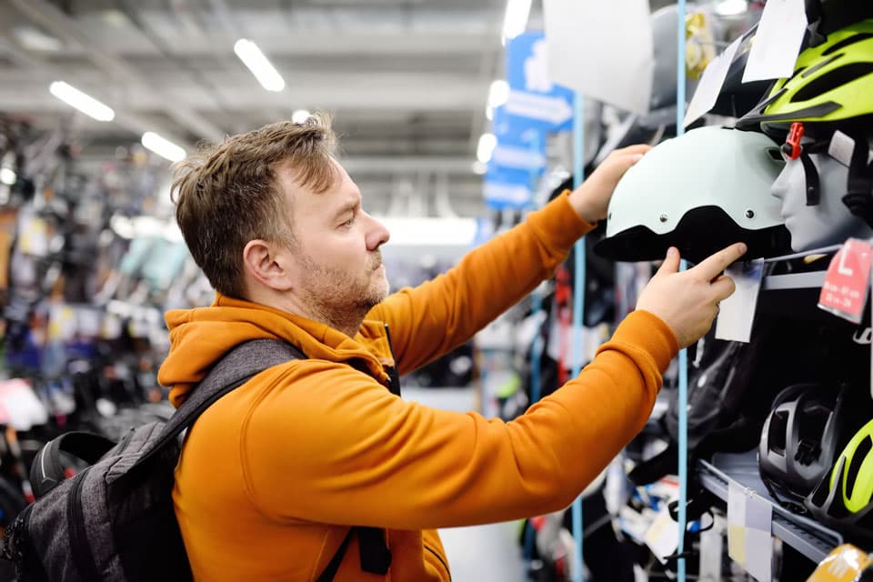 Sporting-Goods-man-choosing-bicycle-helmet-in-sport-store